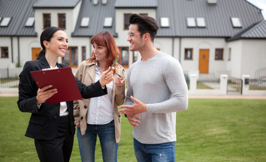 Young couple with real estate agent visiting house for sale in residential area