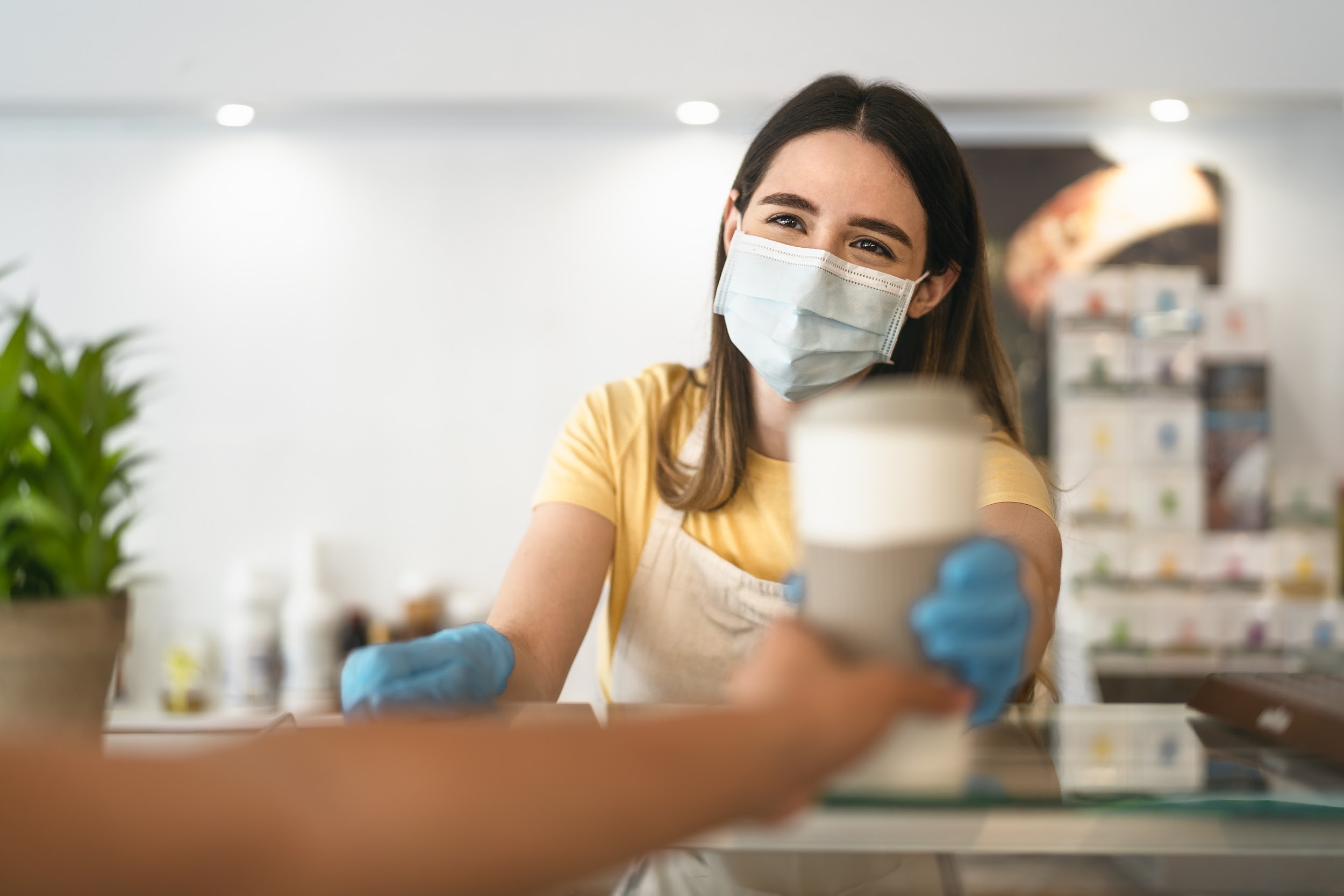 Young woman worker wearing face mask giving coffee to customer