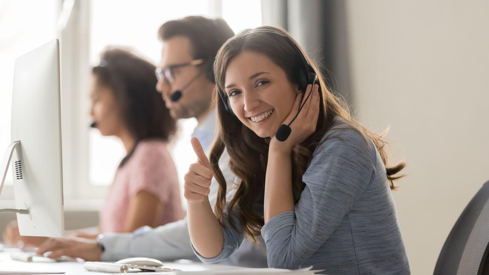 Smiling woman call center operator in headset showing thumbs up gesture