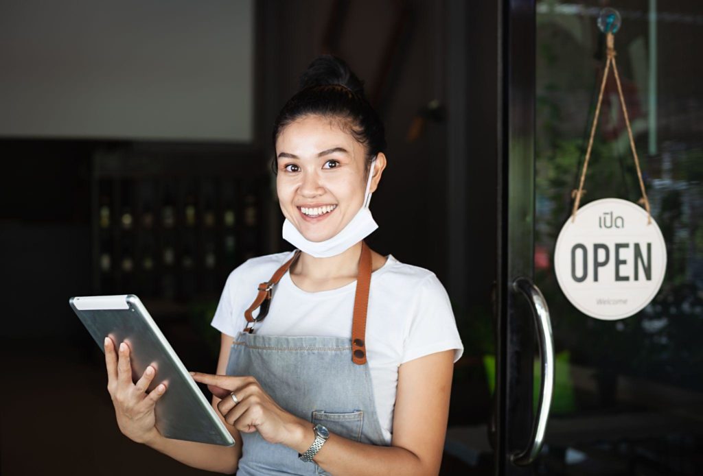 Happy waitress with protective face mask, holding a tablet, restaurant reopening