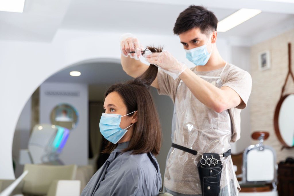 Man doing haircut for woman in salon using face masks