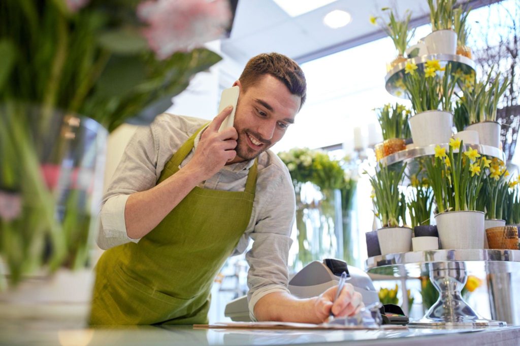 man with smartphone making notes at flower shop