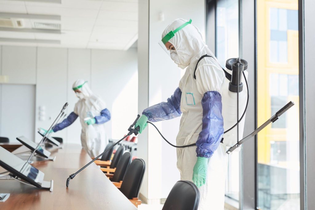 Two workers wearing hazmat suits disinfecting conference room in office