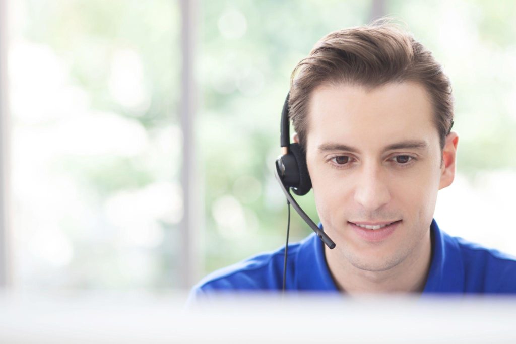 call centre. close up smiling handsome young male operator working with headset in front of computer screen.